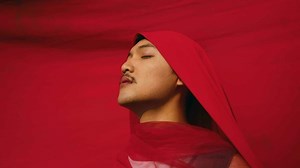 an Asian man bound and strangled by a red cloth with a resigned face in front of a red background