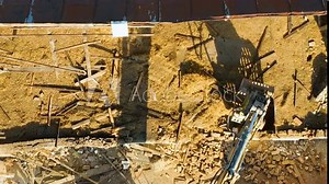 Top-down view of an excavator claw clearing wooden debris on a construction site, showing the aftermath of a demolition