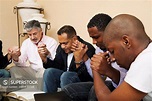 a group of men praying together with an open bible - SuperStock