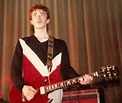 a man standing in front of a red and white guitar