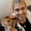 a man holding a violin in his right hand and smiling at the camera ...