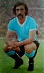 a man with a moustache sitting on the grass in front of a stadium