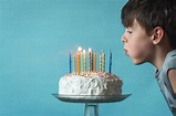 Boy blowing out candles on a birthday cake against blue background ...