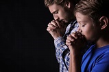 Praying father and son on dark background - Blue Ridge Christian News