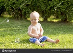 Toddler kid sitting on the grass and playing with bubble blower. Cute ...
