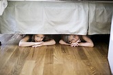 Boy and girl hiding under bed stock photo
