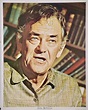 an old photo of a man in front of bookshelves with his mouth open