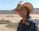a woman wearing a cowboy hat standing in front of some rocks and desert ...