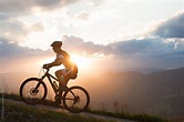 Man riding a bike uphill against sunset sky - Stock Image - Everypixel