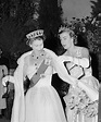 two women in dresses and tiaras standing next to each other