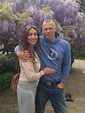 two people standing next to each other in front of purple flowers