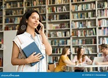 Young Woman with Books Talking on Phone in Library Stock Photo - Image ...