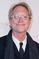 an older man wearing glasses and a polka dot scarf smiles at the camera ...