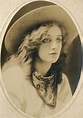 an old black and white photo of a woman wearing a hat with her hair blowing in the wind
