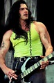 a man with long hair holding a guitar and wearing a green tank top on stage