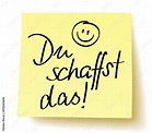 Quadratisches gelbes Postit mit der Handschrift: „Du schaffst das!“ und ...