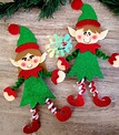 two christmas elfs made out of felt on a wooden table with pine ...