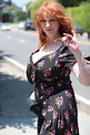 a woman with red hair is standing on the side of the road and holding ...