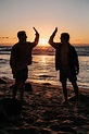 silhouette of two mens near seashore about to high five during sunset ...