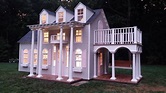 a doll house is lit up at night in the yard with porches and columns