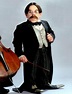 a man in a tuxedo and bow tie holding a cello while standing next to an ...