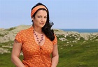 a woman in an orange shirt and headband standing on the side of a hill