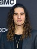 a man with long hair wearing a suit and black t - shirt at an event
