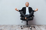 Relaxed african young man sitting and meditating on office chair ...