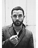 a black and white photo of a man with a beard wearing a suit jacket ...