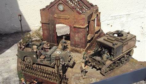 a toy tank with soldiers standing next to it in front of a small brick