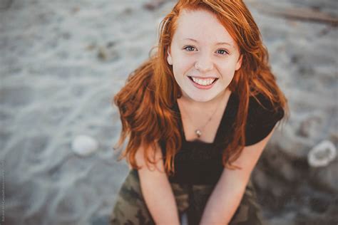 Happy Portrait Of Redhead Teenage Girl Sitting At The Beach By Stocksy Contributor Rob And
