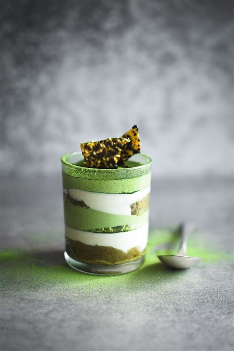 A Green And White Dessert In A Small Glass With A Spoon Next To It On A Gray Surface