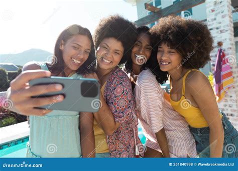 Carefree Biracial Female Friends Taking Selfie Over Cellphone While Having Fun At Poolside In