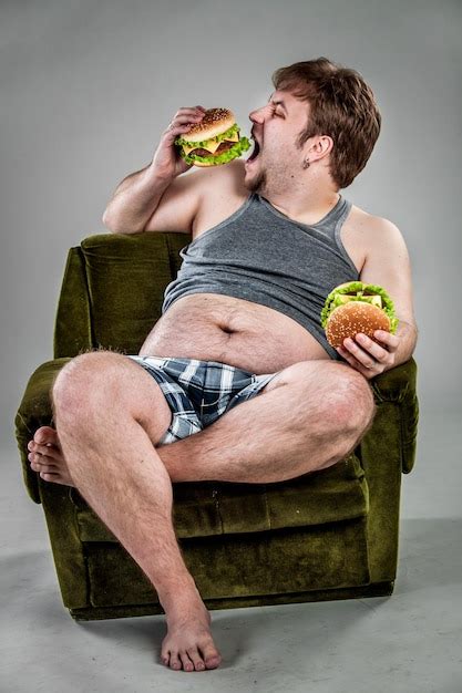 Толстяк ест гамбургер сидя на кресле стиль фаст фуд Премиум Фото