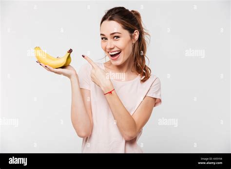Portrait Of A Cheerful Young Girl Holding Bananas And Pointing Finger