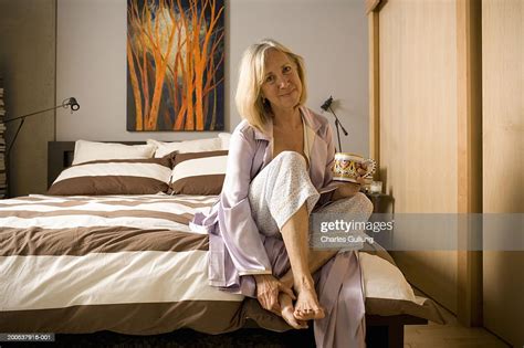 Mature Woman With Coffee Mug Sitting On Edge Of Bed Portrait High Res