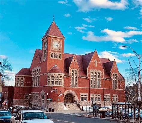 A Large Red Brick Building With A Clock On Its Side And Cars Parked In