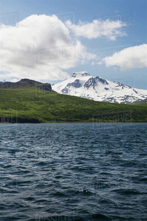 Green Shores And Snow Covered Roundtop Mountain On Unimak Island The
