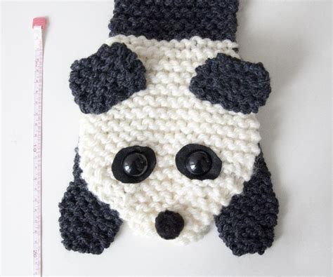 A Crocheted Panda Bear With Black And White Eyes Is Next To A Ruler
