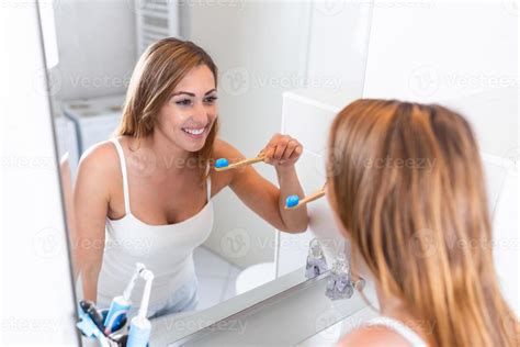 Pretty Female Brushing Her Teeth In Front Of Mirror In The Morning