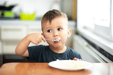 A Little Boy In The Kitchen Greedily Eats Rice With A Spoon Stock Image