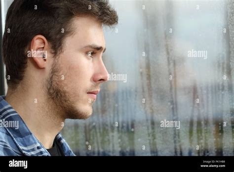 Side View Of A Man Longing And Looking Through Window In A Sad Rainy