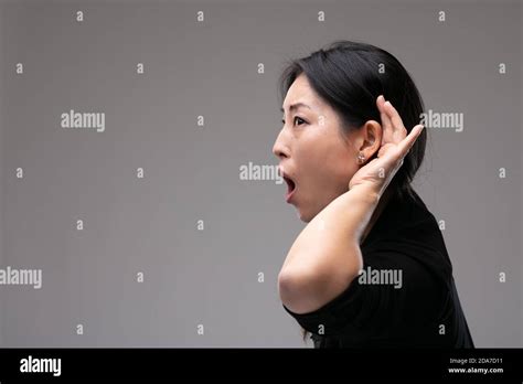 Asian Woman Eavesdropping And Holding Her Hand To Her Ear Reacting In Shock And Amazement With