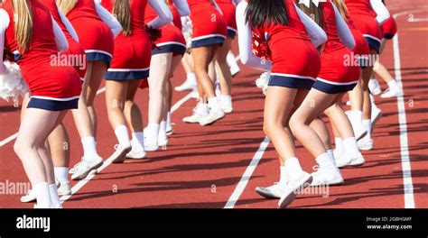 High School Cheerleaders Wearing Red Uniforms Cheering On The Sidelines Using Pom Poms During A