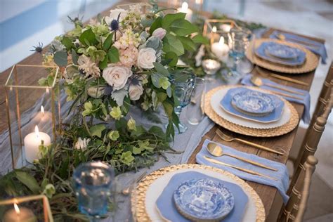 The Table Is Set With Blue And White Plates Silverware Greenery And