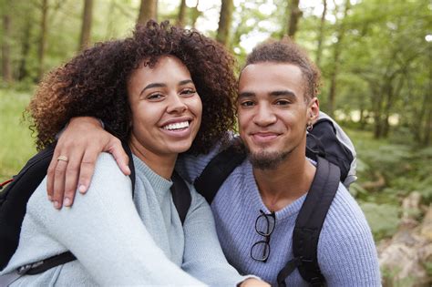 A Young Mixed Race Couple Smiling To Camera During A Hike In A Forest