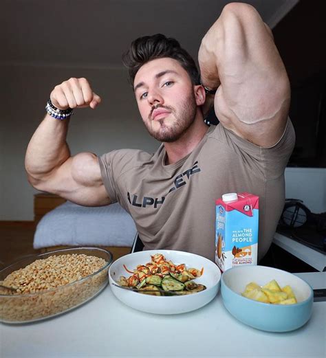 A Man Flexing His Muscles While Sitting At A Table With Bowls Of Food On It