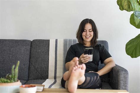 Woman Sitting On Couch With Feet Up On Phone Lizenzfreies Stockfoto