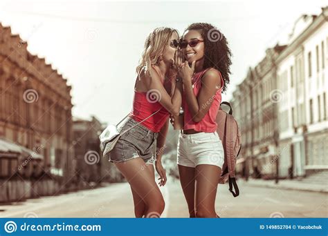 Delightful Lady Whispering In Ear Of Her Curly Haired Girlfriend Stock