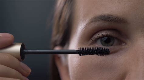 Close Up Shot Of Young Woman Applying Mascara On Eyelashes Against